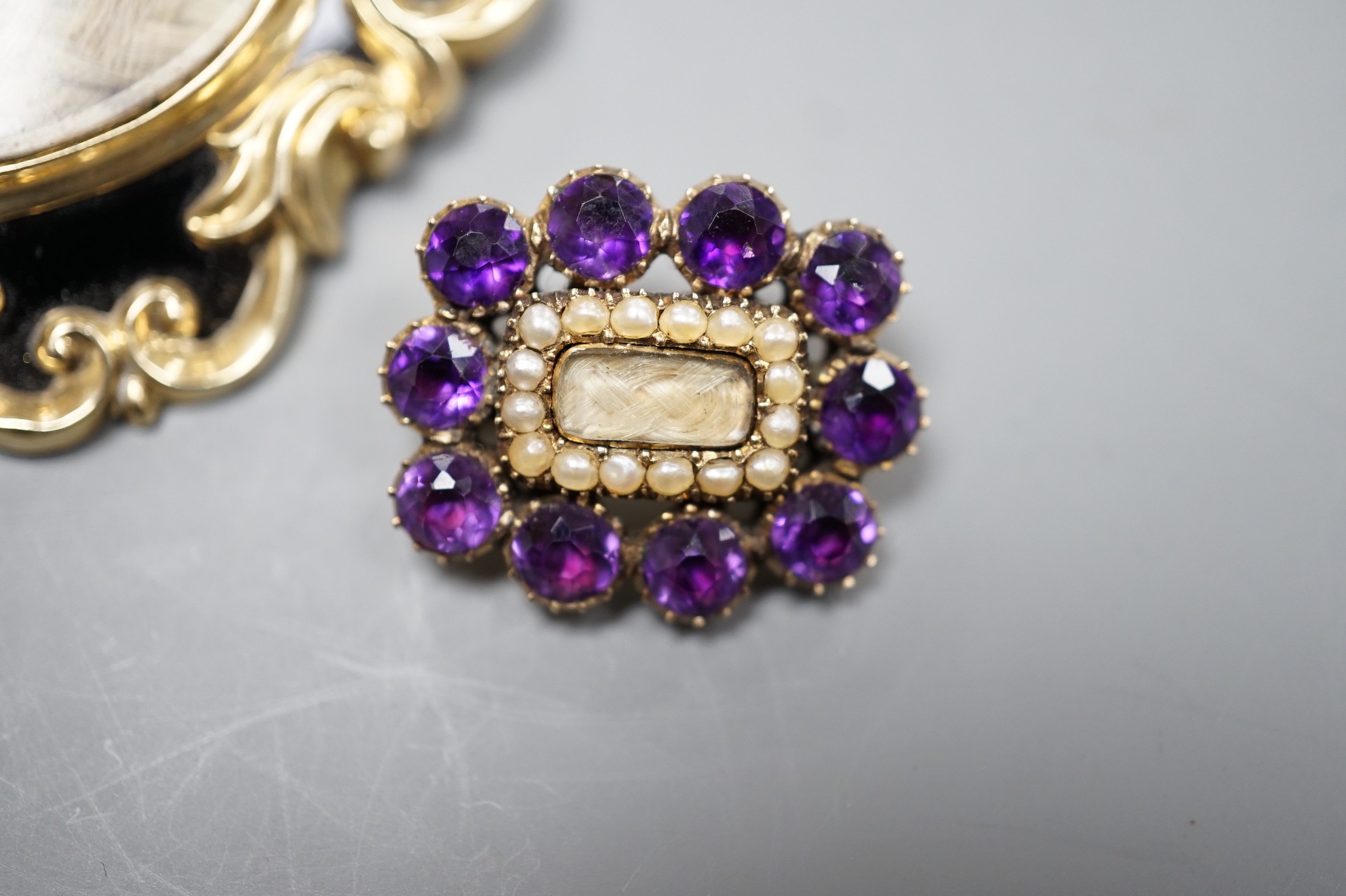 Two Victorian yellow metal (tests as 9ct) mourning brooches, one with black enamel and pendant bale, 51mm, the other with amethyst and seed pearl, both with plaited hair beneath a glazed panel.